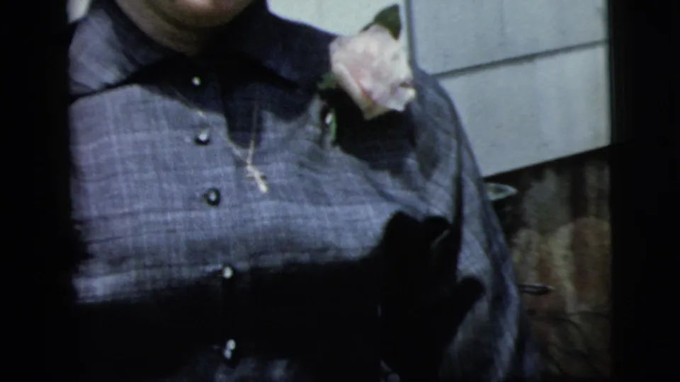 1958 New York City 8mm frame showing a cropped close view of a young woman in a dark collared blouse with a pale rose corsage.