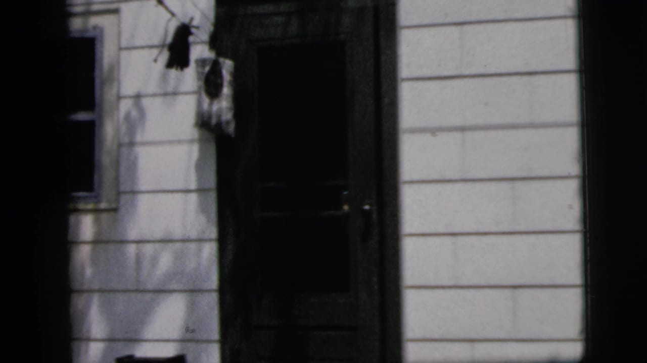 Light-sided house exterior with a dark doorway and film-gate borders.