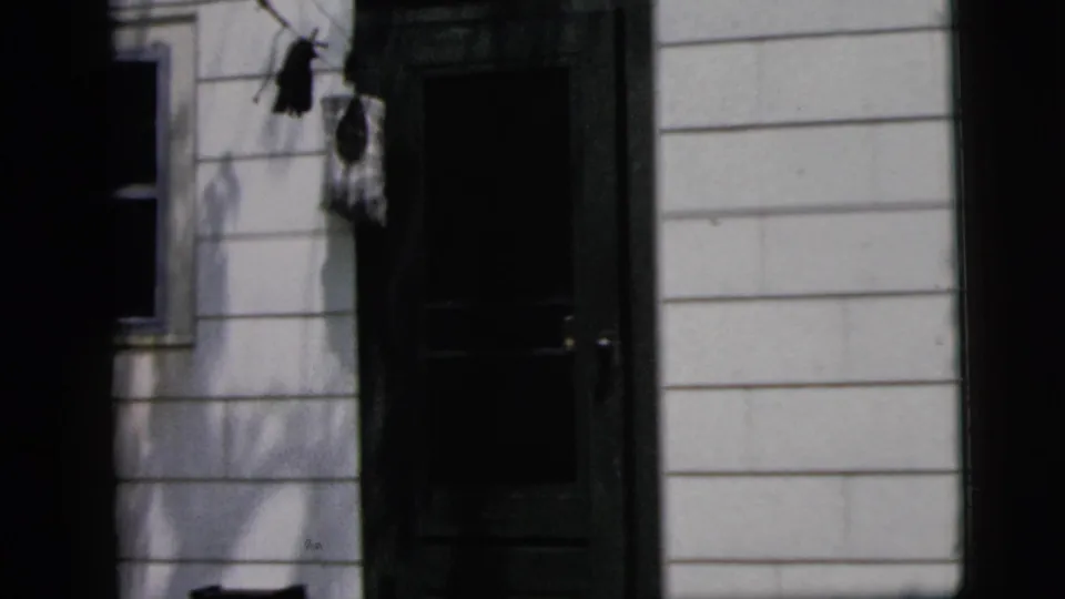 1958 New York home-movie frame showing part of a light-sided house exterior, a dark doorway, window edge, and strong film-gate borders.