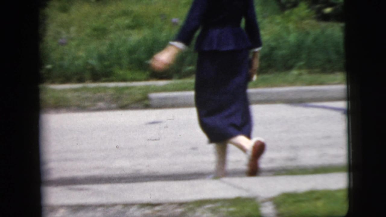 Woman in dark blue clothing walks across a road carrying a small handbag.