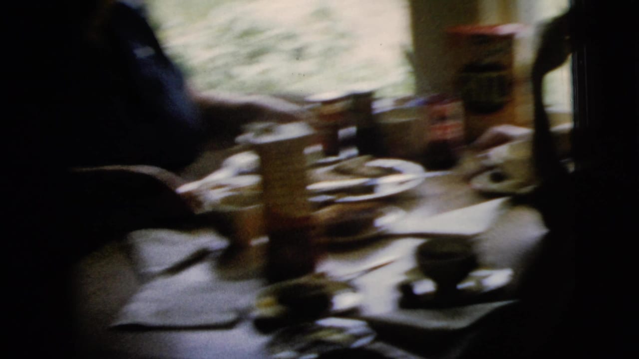 Tabletop with cups, plates, hands, and a cracker box in a dim home interior.