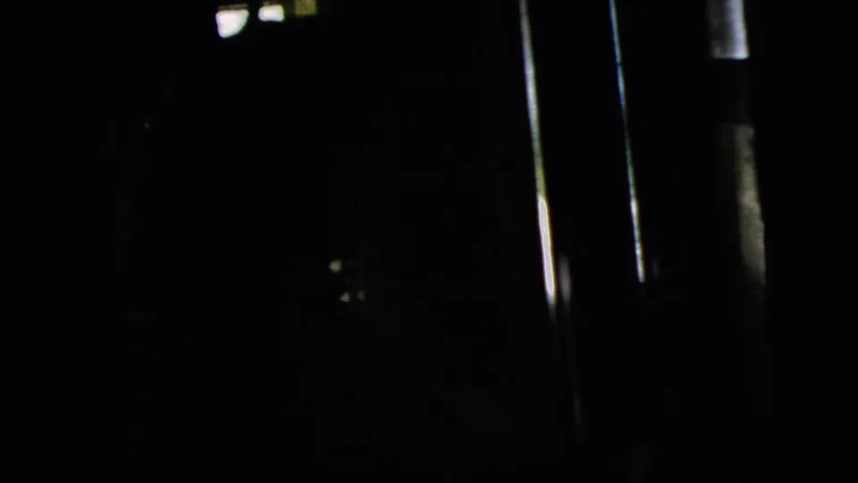 The final 1958 home-movie frame falls mostly into shadow, with slim bright window strips and indistinct interior details.