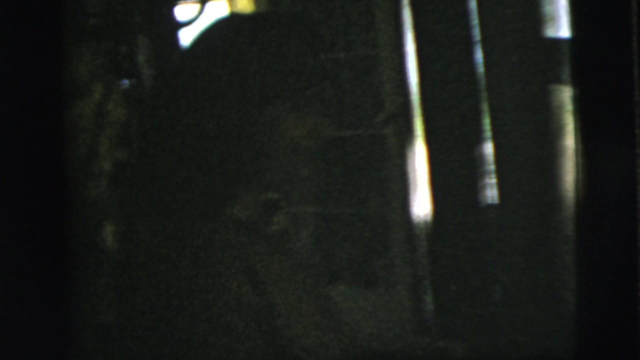 Dark, partially obscured frame with building reflections and a couple near a doorway at right.