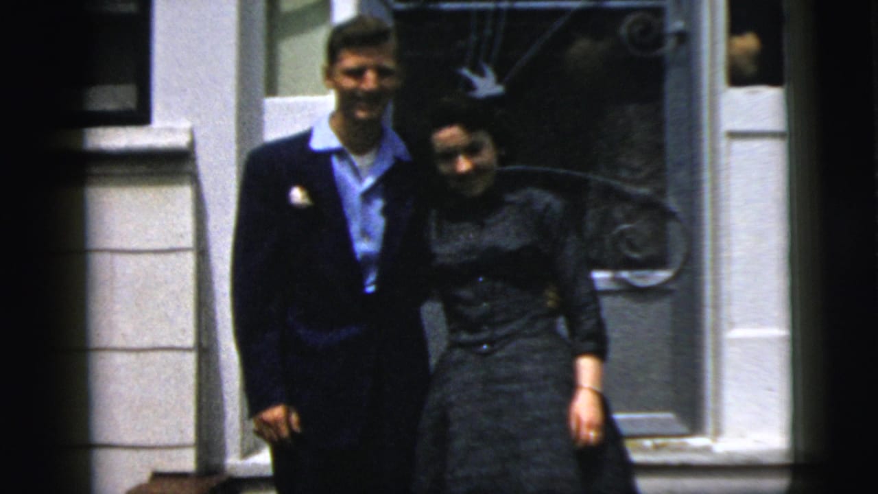 A young couple in 1958 New York City stands close together outside a white-trimmed doorway in soft 8mm color footage.