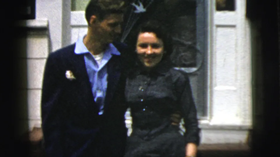 A closer 8mm frame shows the man and woman standing arm in arm outside a white-trimmed doorway in New York City.
