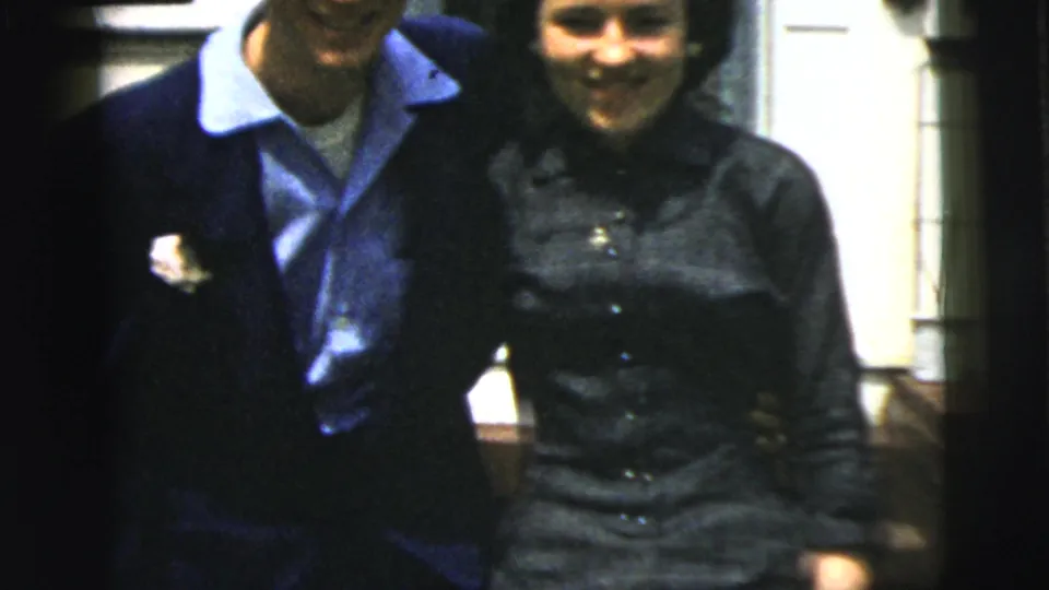 A closer home-movie frame shows the dressed-up couple smiling together, cropped tightly against the house exterior.