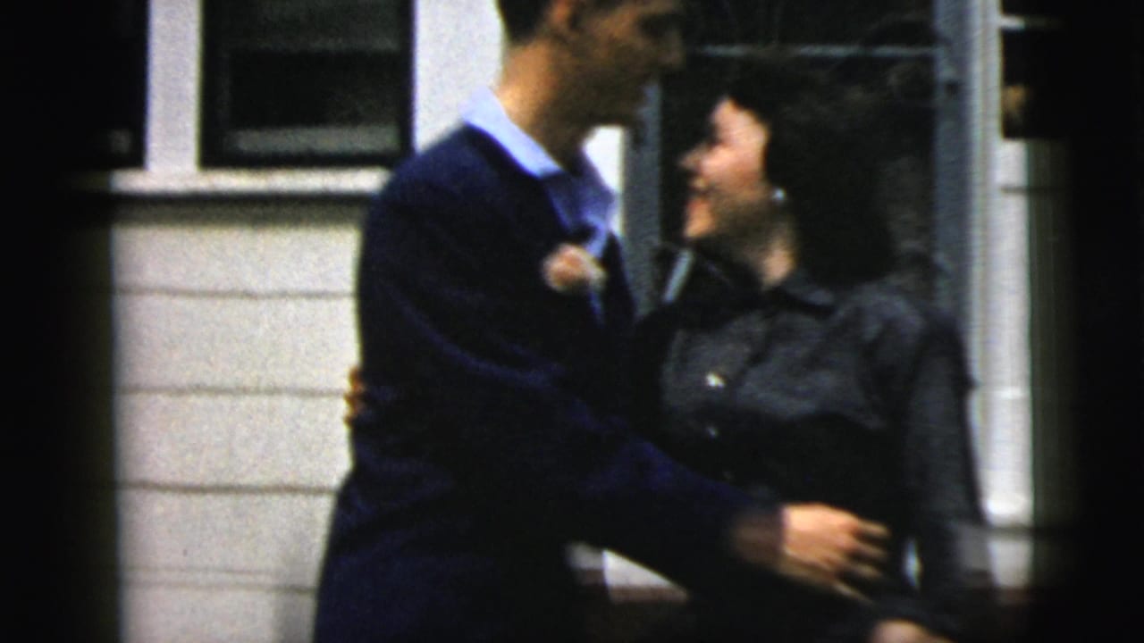 Young couple in formal clothing smiling and holding each other outside a house.