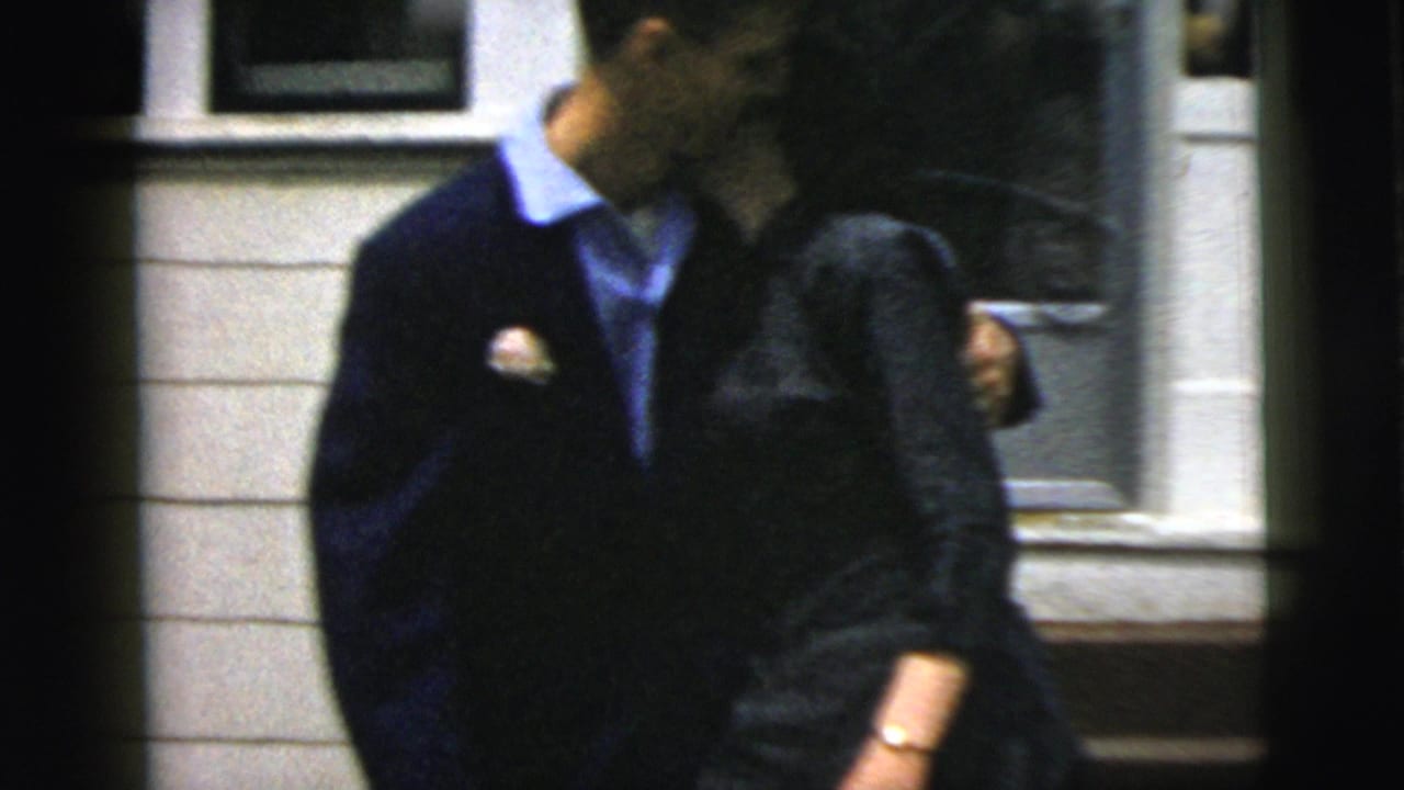 Couple leaning close and kissing beside a residential doorway.