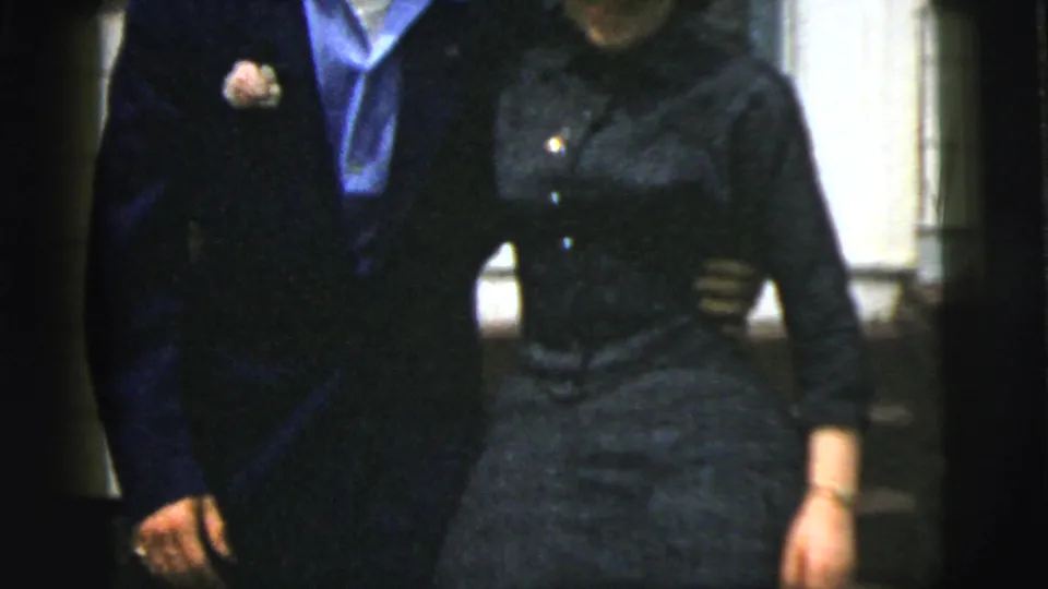 A closer 8mm frame shows the man's boutonniere and light blue shirt beside the woman's dark dress as they stand arm in arm.