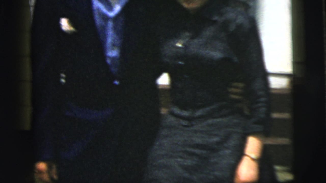 Well-dressed couple standing close near a doorway, partly blurred by handheld 8mm motion.