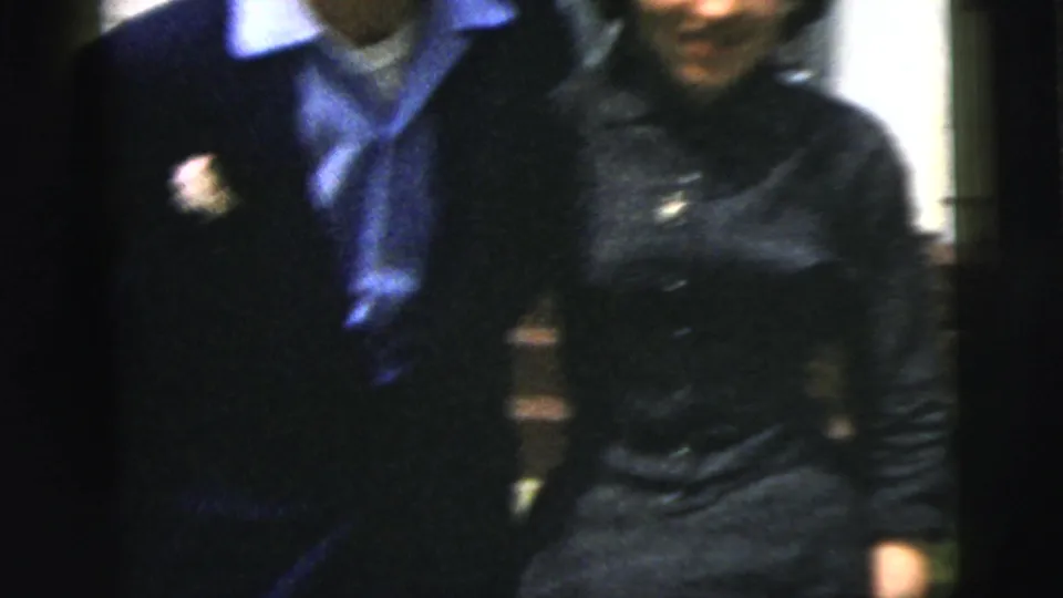 The 1958 New York City home-movie frame shows a close view of the couple’s formal clothing, including a boutonniere, blue collar, and dark dress.