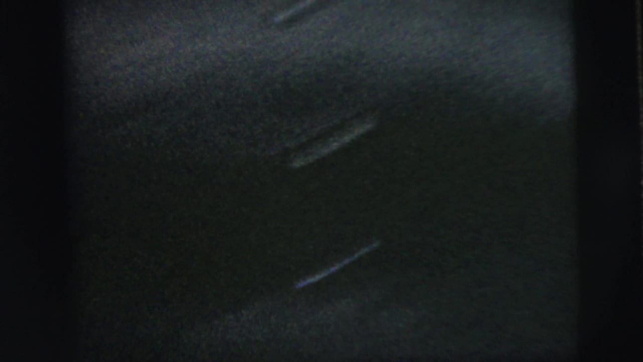 Soft, dark 8mm frame showing only a partial residential exterior and heavy contact-sheet border obstruction.
