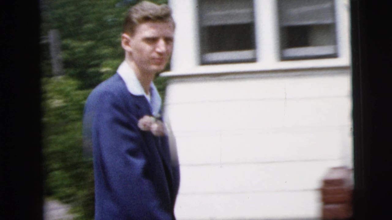 Teenage boy in a blue suit and white shirt, with a lapel corsage, walking outside a New York City house in 1958 footage.