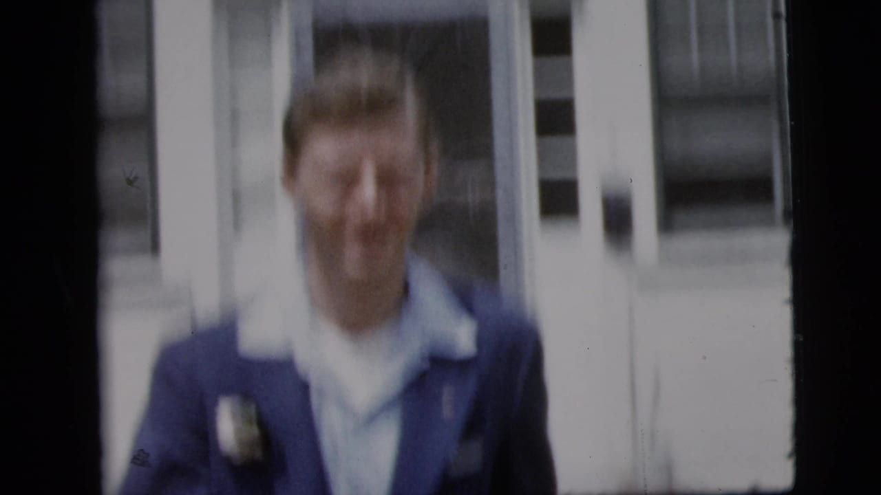 In 1958 New York City home-movie footage, a smiling man in a blue suit with a boutonniere appears near a building entrance.