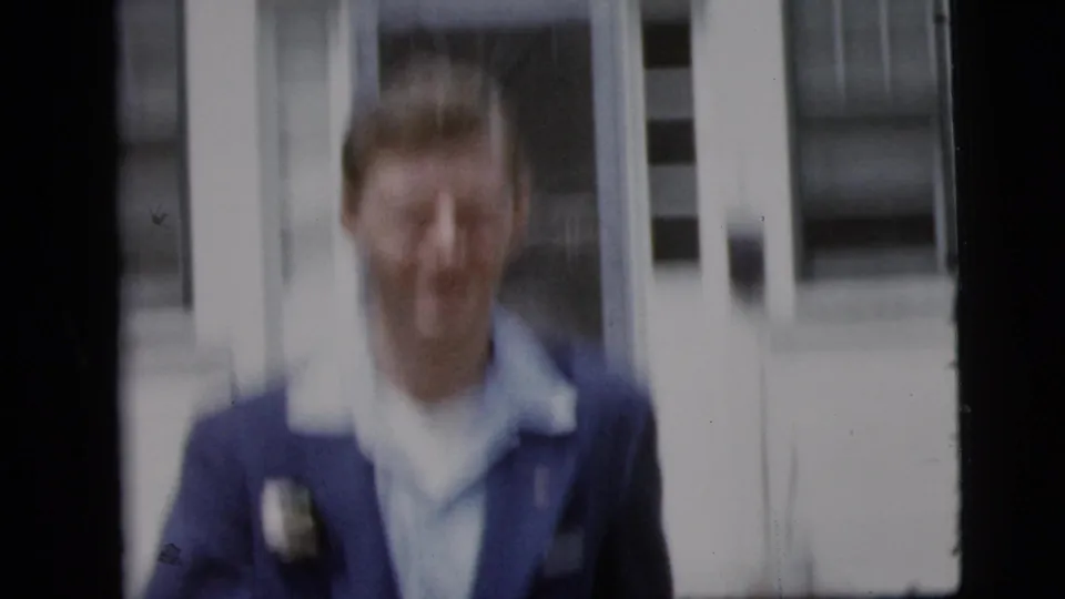 In 1958 New York City home-movie footage, a smiling man in a blue suit with a boutonniere appears near a building entrance.