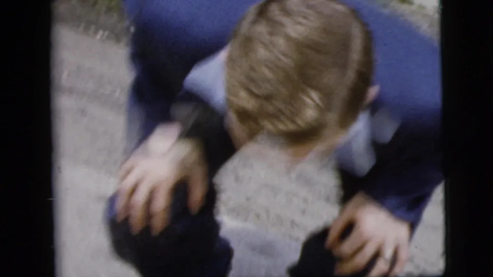 From a high handheld angle, the man in the blue suit leans or crouches near the camera, his hair, hands, and suit visible.