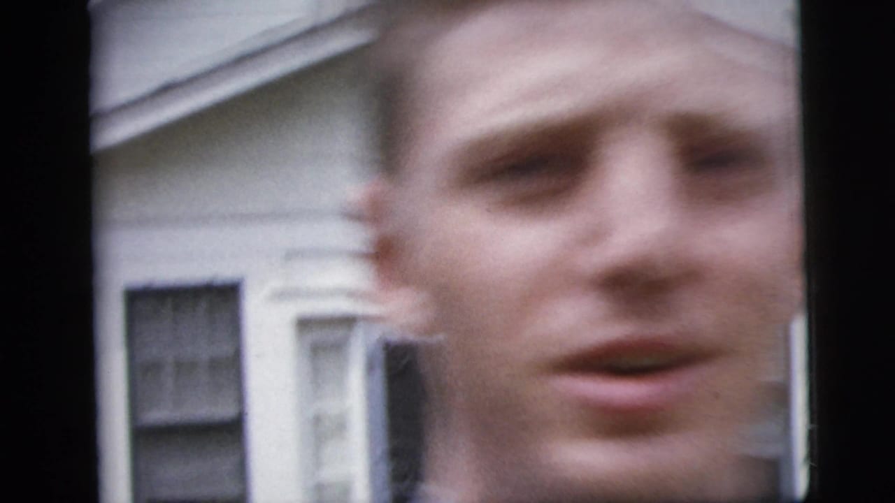 Soft-focus 1958 New York City home-movie frame with a young man close to the lens near a house facade.