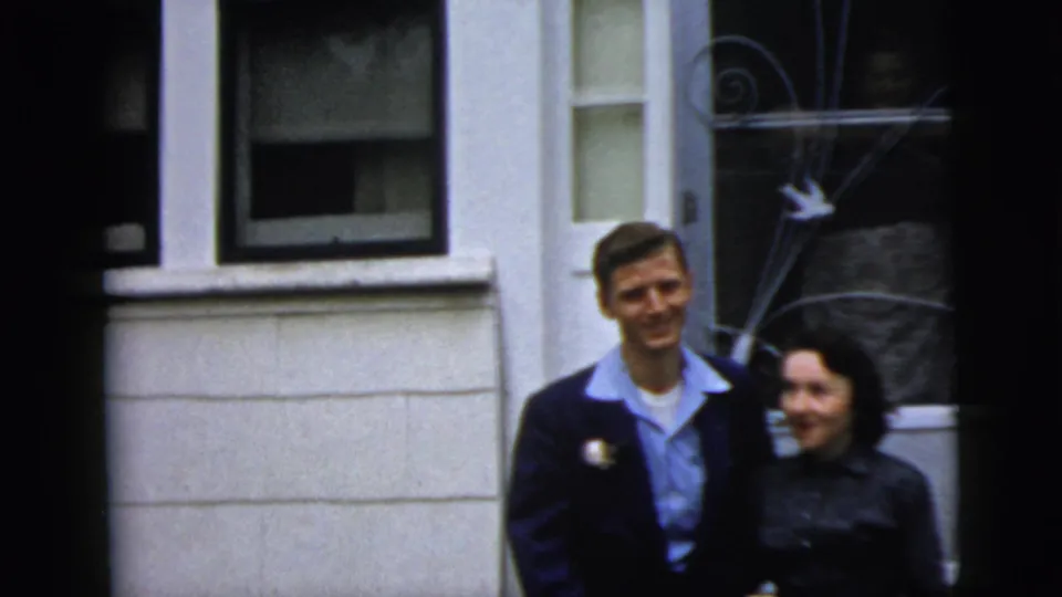 The formally dressed couple walks side by side from a New York City house entrance in 1958 home-movie footage.