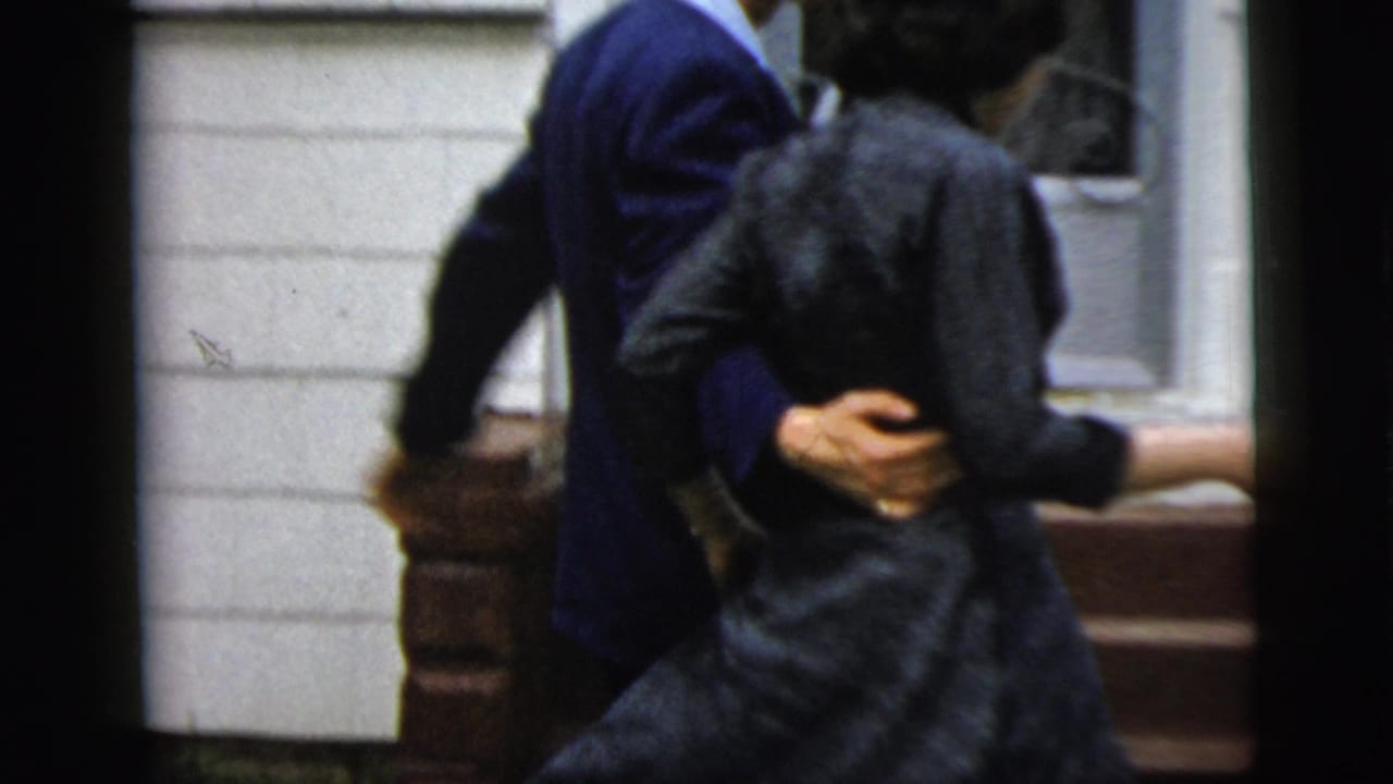 The couple turns together beside brick steps, with the man in a navy suit guiding the woman in a dark dress.