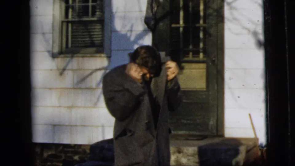 The man in a dark overcoat looks down and adjusts his collar outside the New York City house.
