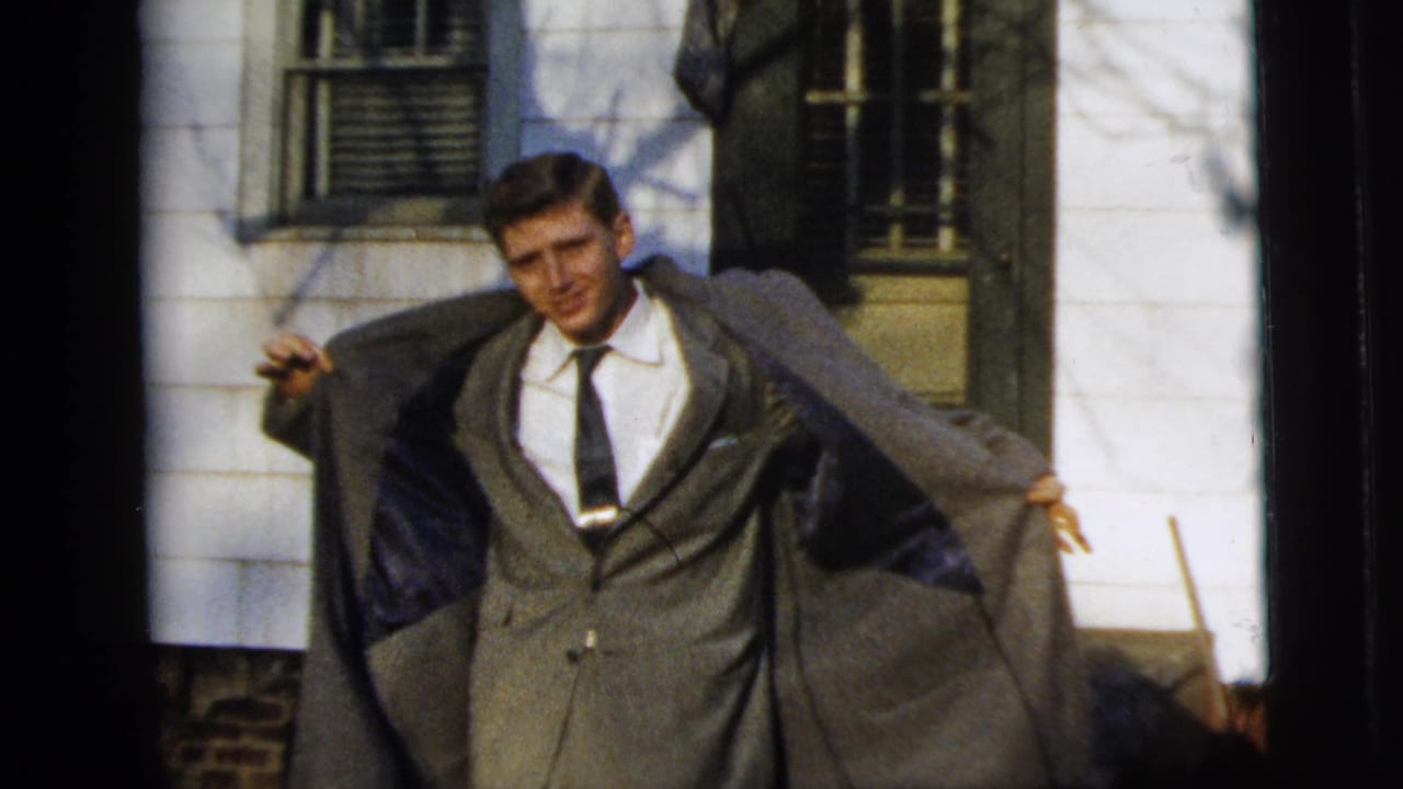 Young man opens his gray overcoat to show a suit and tie.