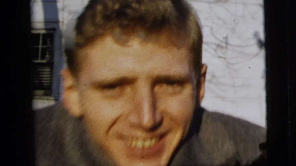 A soft close-up from the 8mm footage shows the smiling man leaning toward the camera outside the New York City house.