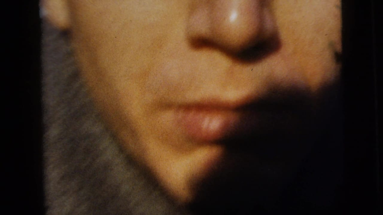 Close 1958 home-movie frame of a young person’s lower face near the lens, with soft focus, shadow, and warm 8mm color.