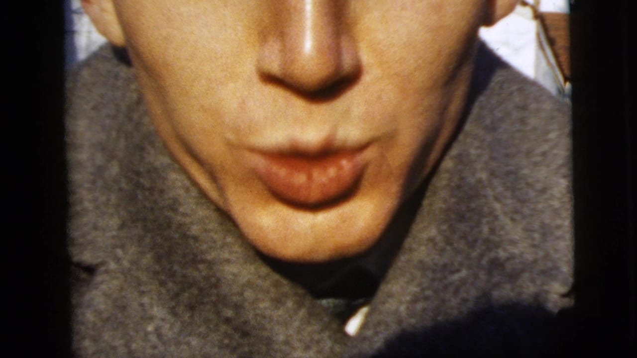 Young man in a gray overcoat puckers toward the camera in a playful 1958 New York City home-movie close-up.