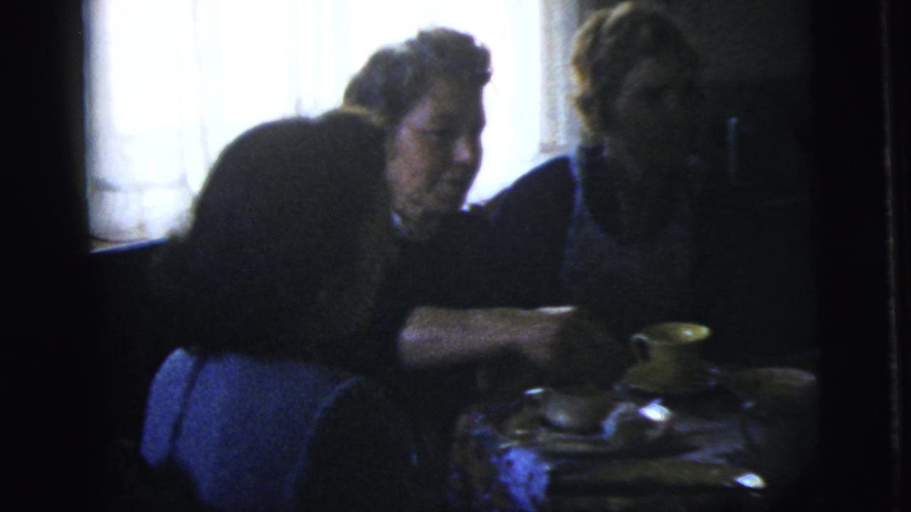 Adults at a table as one person reaches toward food near yellow cups.