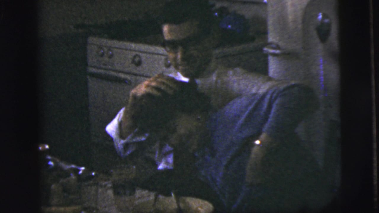 Man leaning over a woman in a dim kitchen near a stove and tableware.