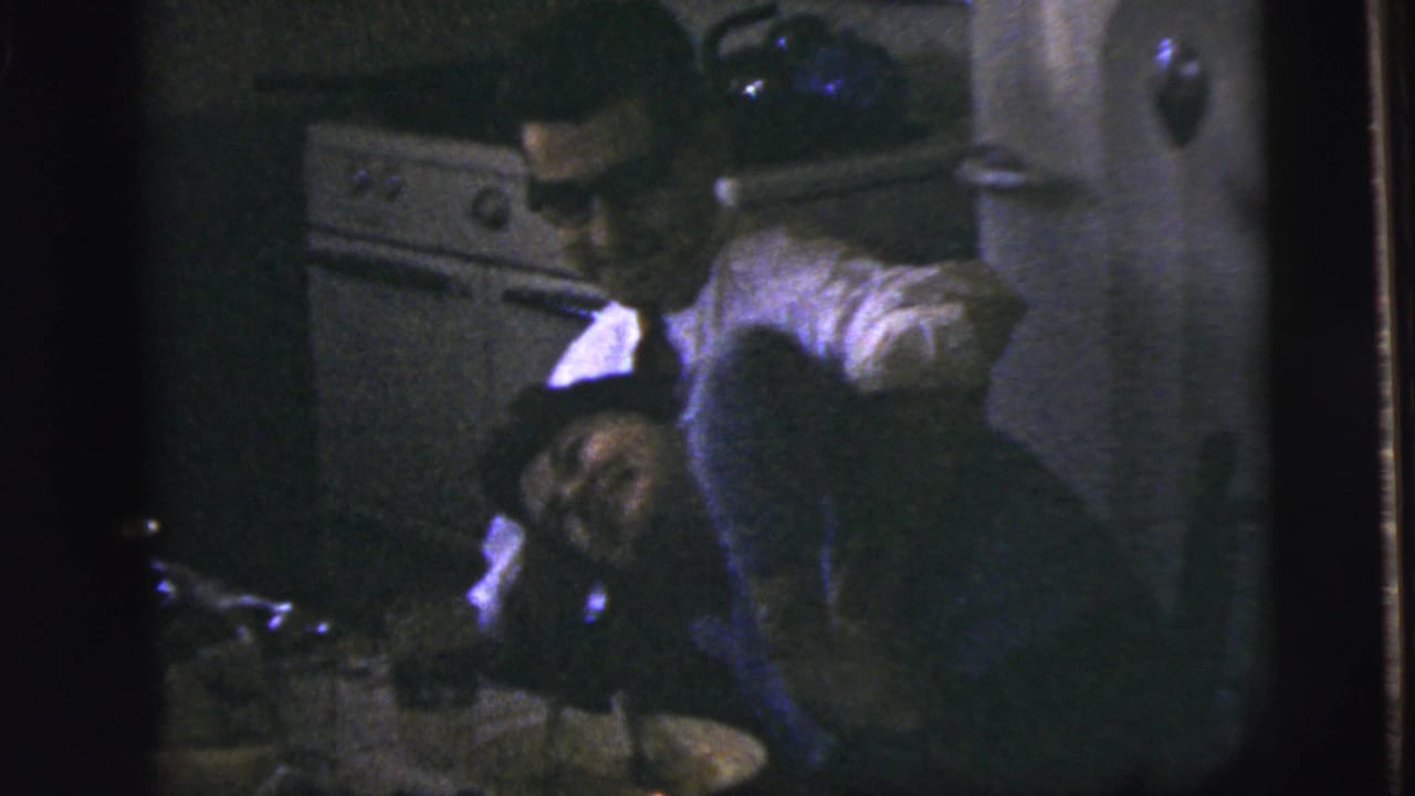 Woman leaning back while a man bends close in a dark kitchen interior.