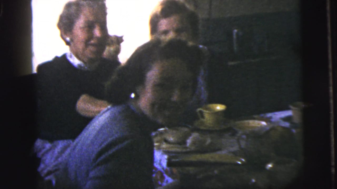 Three adults seated around a dim kitchen table with cups and plates.