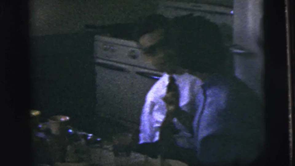 A man in a shirt and tie turns beside a kitchen table in 1958 New York City home-movie footage.