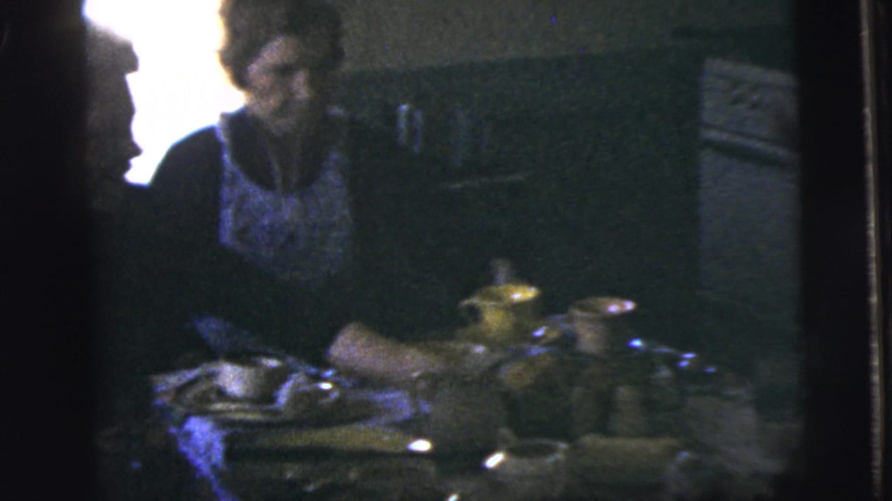 Adults seated at a dining table with plates and cups in a dim kitchen interior.