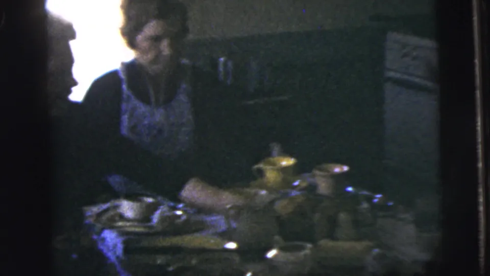 1958 New York City home-movie frame showing adults gathered at a dining table with tableware in a private kitchen interior.