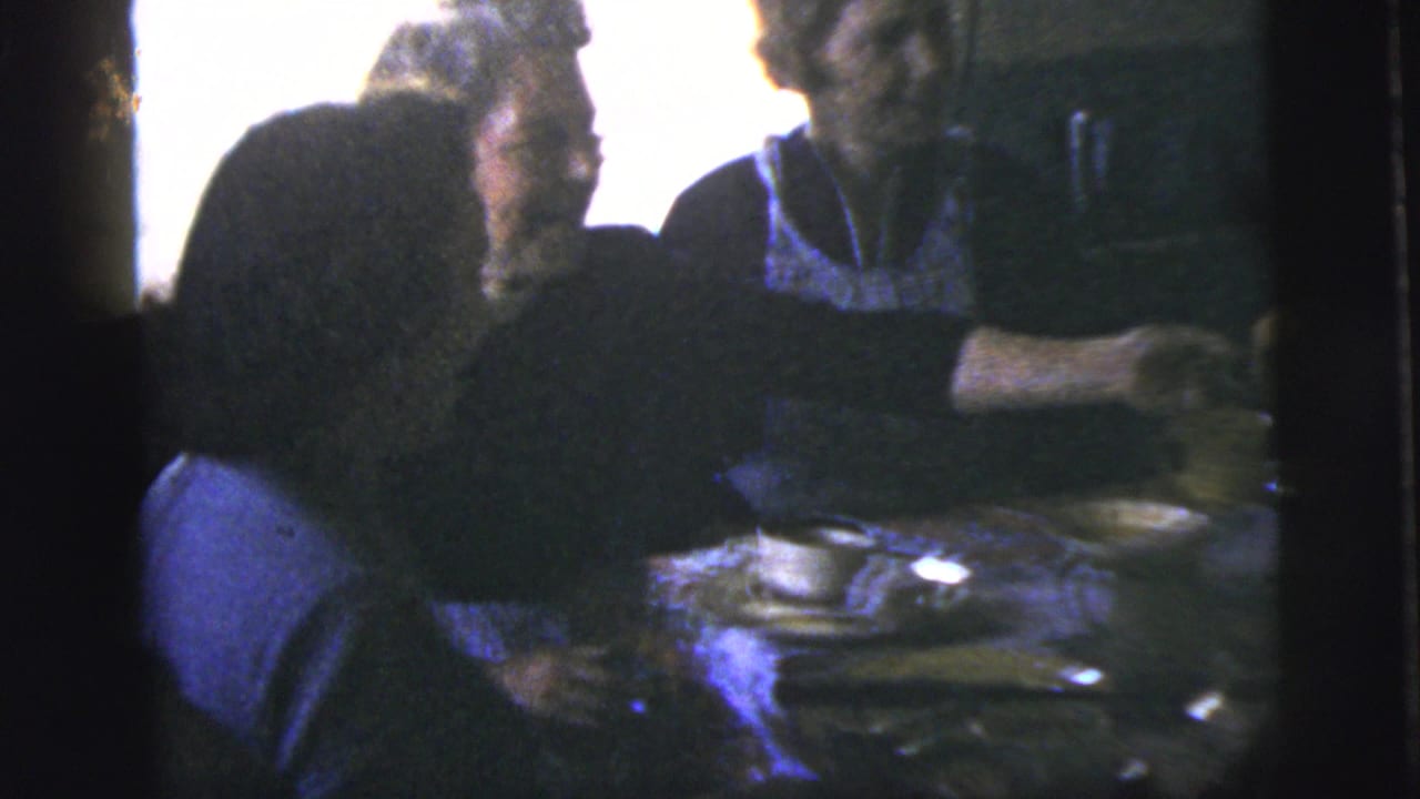 Home-movie frame from the 1958 New York City clip showing adults seated closely around a dining table during a meal.