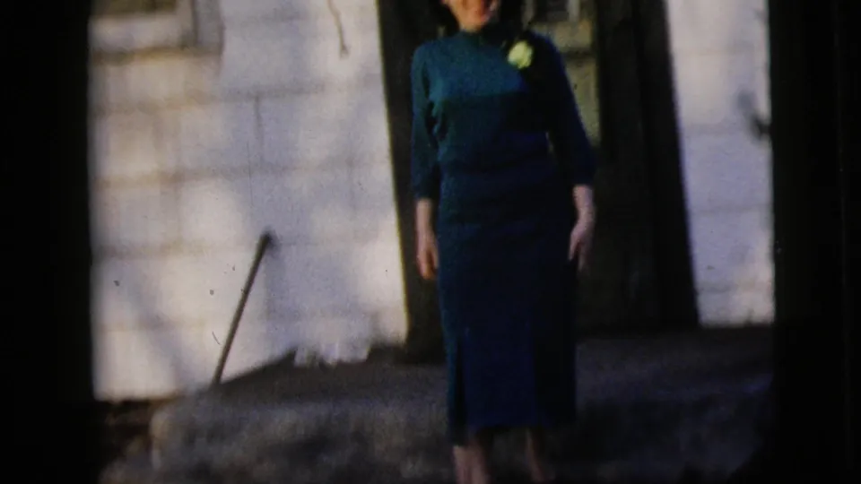 1958 New York City home-movie frame of a young woman in a teal dress descending or standing near stone house steps.