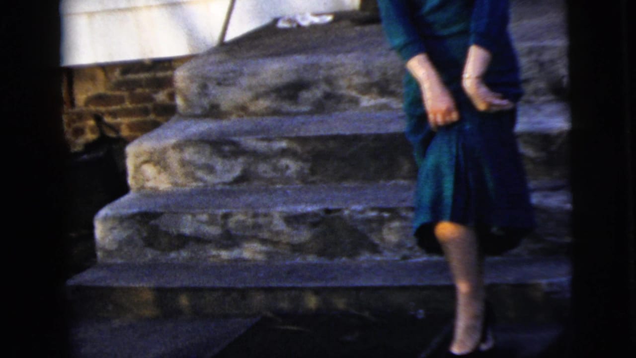 Woman in a blue dress standing on stone steps outside a house.