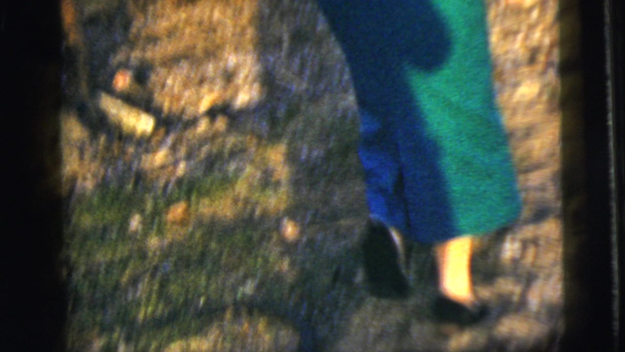 Lower view of a woman walking across grass and leaves in dark heels.