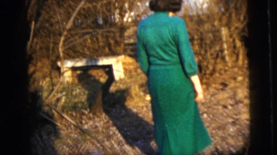 Adult woman in a green dress stands with her back to the camera in a New York City garden setting, 1958 home-movie footage.