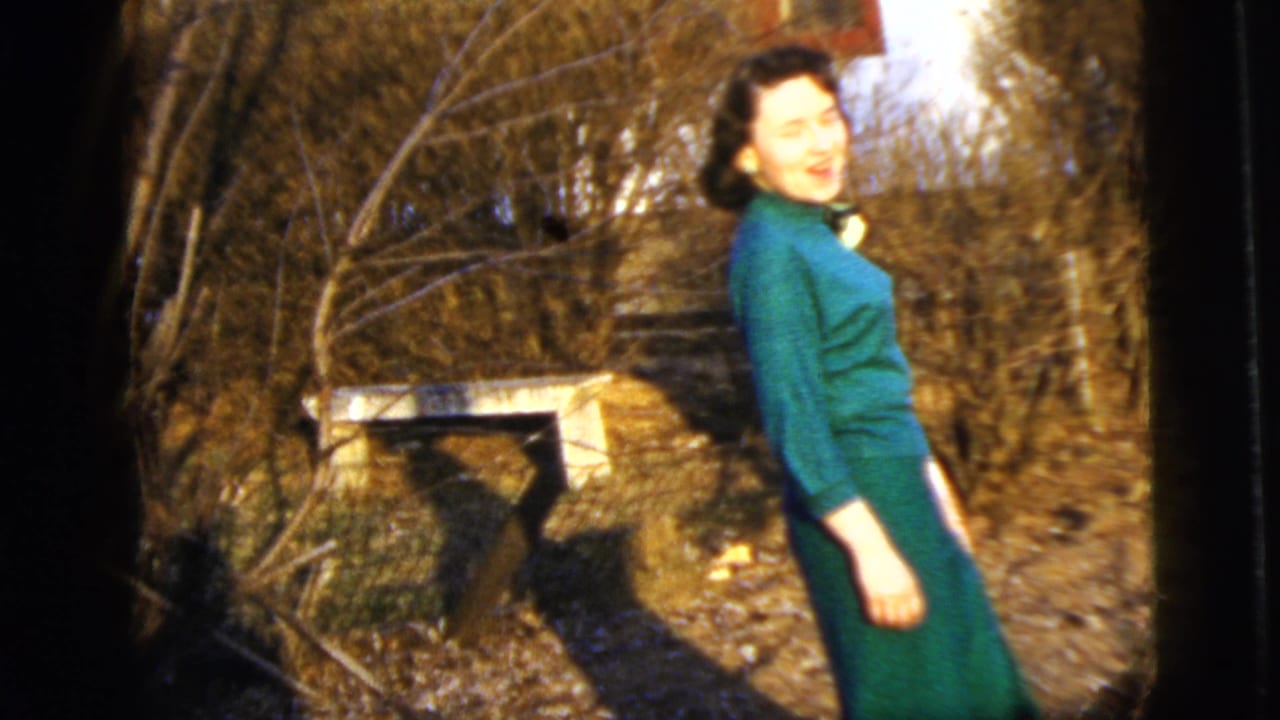 Woman in green turns toward the camera and smiles in a garden.