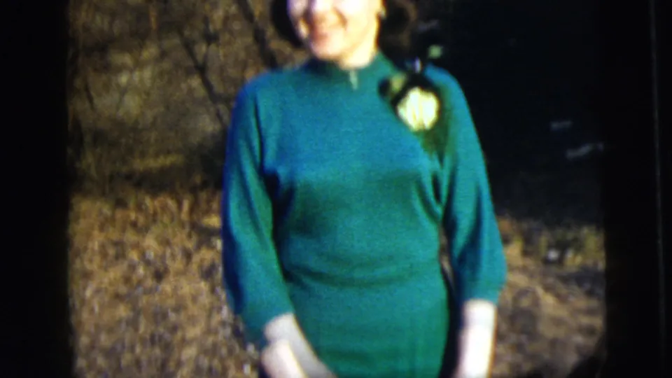 A closer soft-focus view shows the woman's green turtleneck dress and white corsage against an outdoor background.