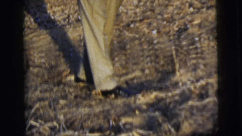 Soft 8mm frame focused on tan trouser legs and dark shoes standing in a dry outdoor area.