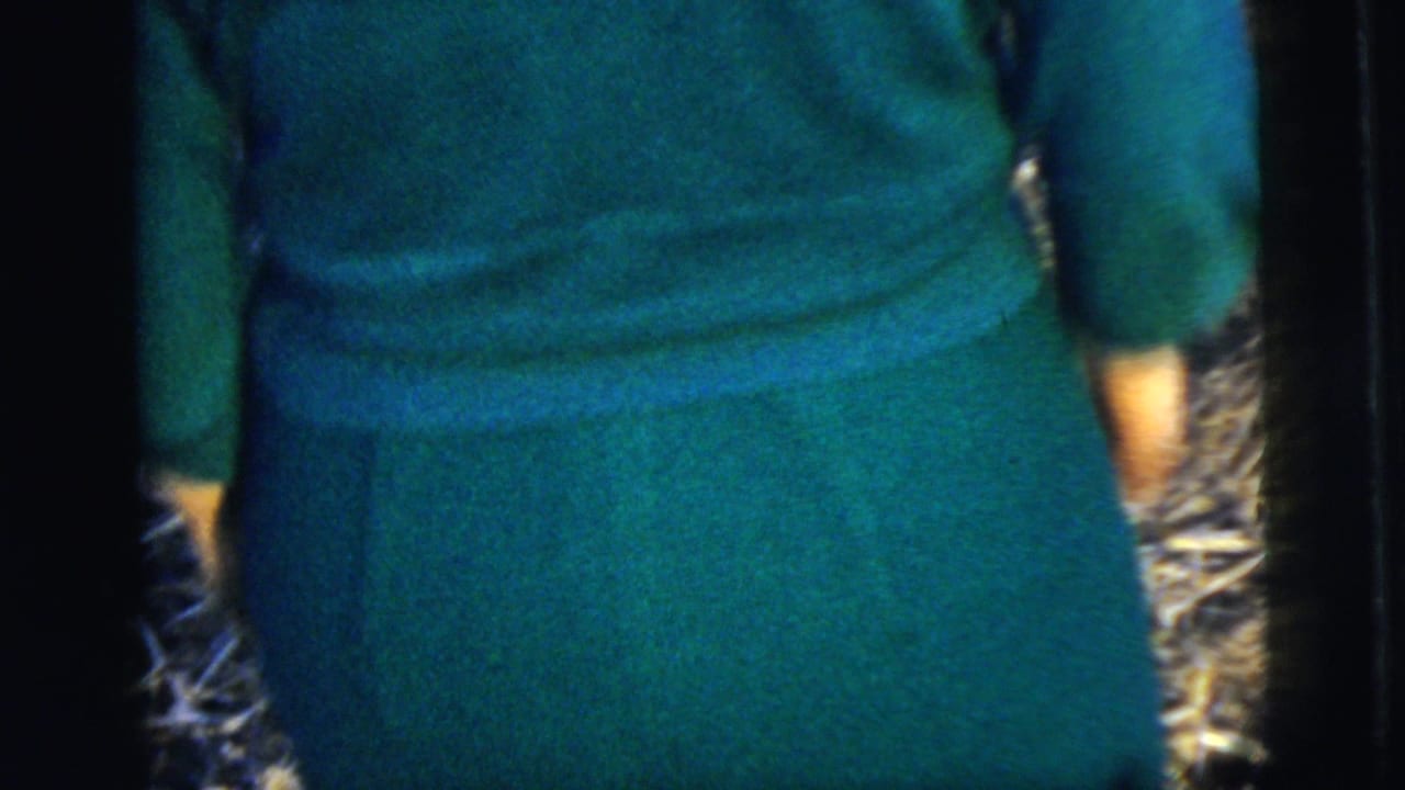 A woman in a teal dress is filmed from behind as she walks outdoors, with the frame tightly cropped around her back and skirt.