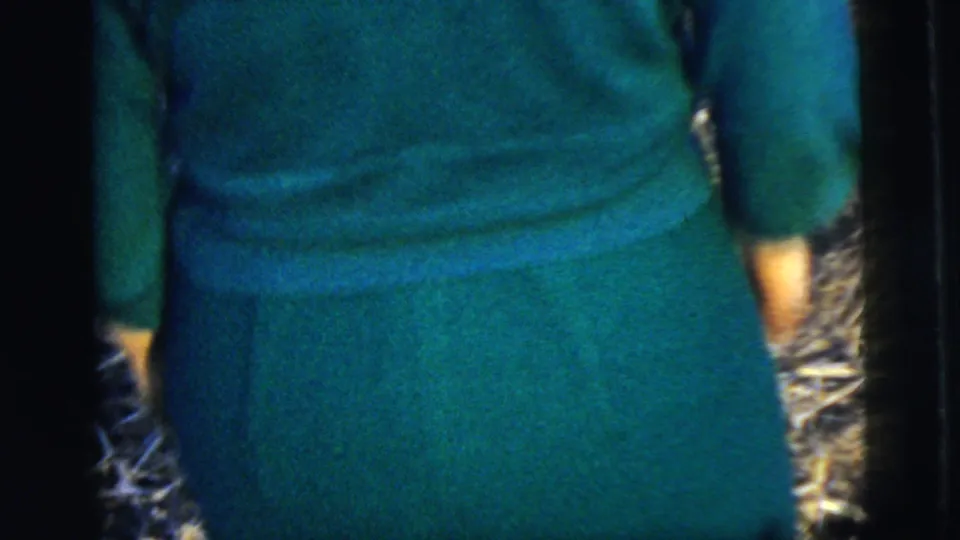 A woman in a teal dress is filmed from behind as she walks outdoors, with the frame tightly cropped around her back and skirt.
