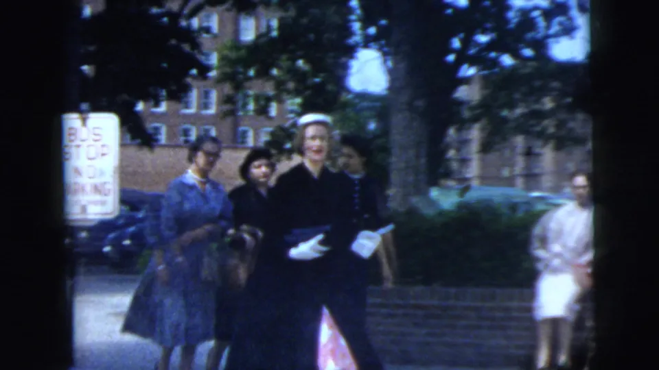 People walk along a New York City sidewalk in 1958 home-movie footage, with brick buildings behind them.