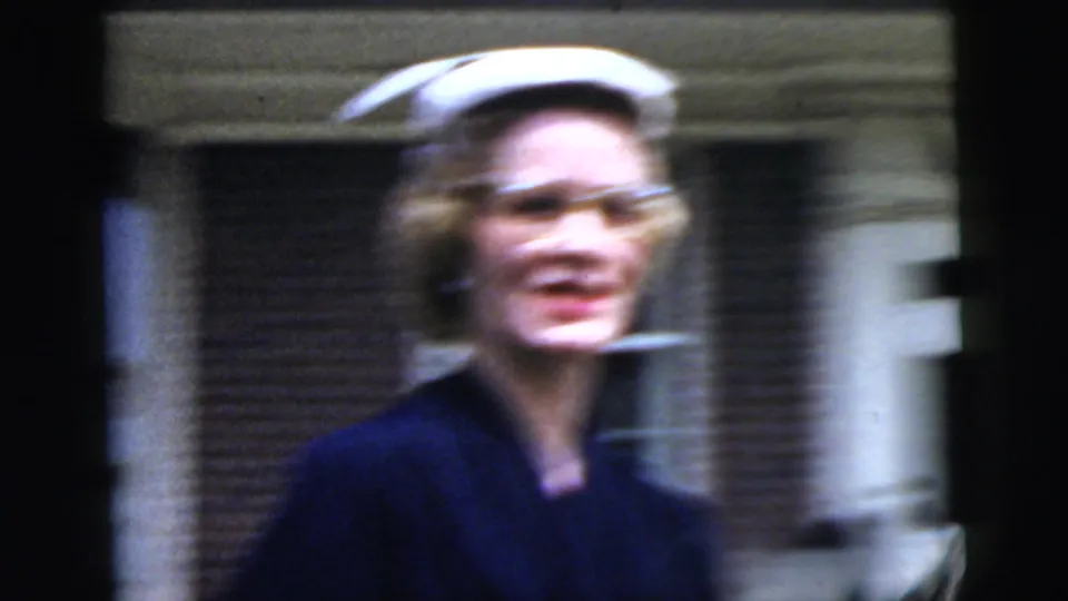 A close handheld frame shows the woman in a white hat moving past brick architecture, with visible motion blur from the 8mm camera.