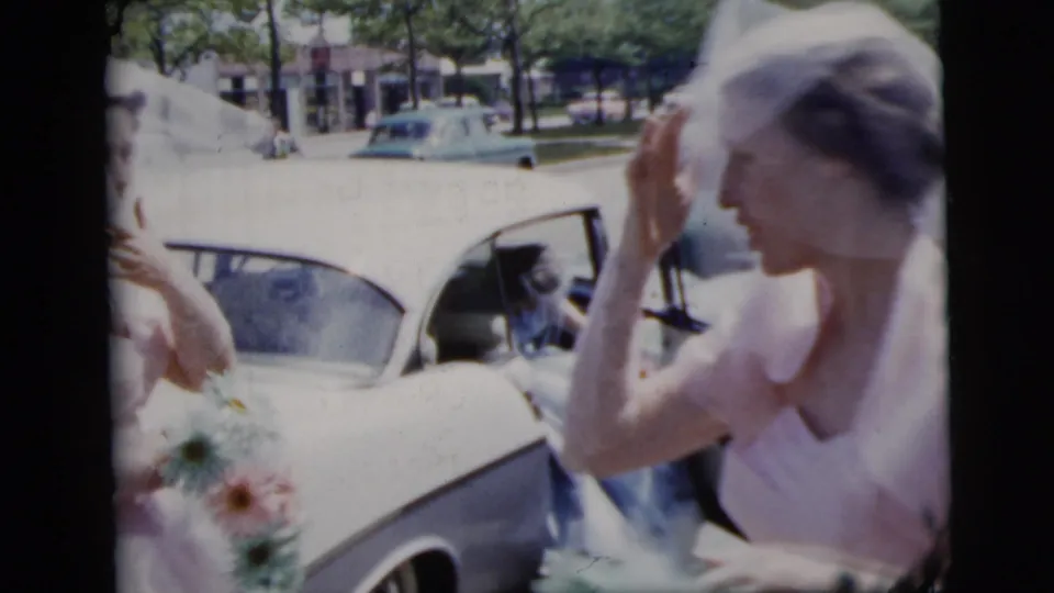 1958 New York City wedding frame showing a veiled bride beside a white car, with attendants and bouquets near the open car door.