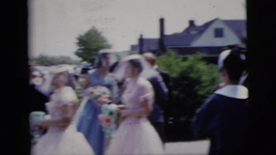 In 1958 New York City home-movie footage, a veiled bride and bridesmaids in pale dresses move past guests along a residential street.