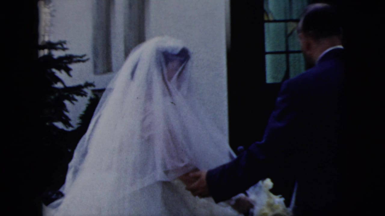 A man in a dark suit appears to guide the veiled bride toward a church entrance in the 1958 New York City wedding scene.